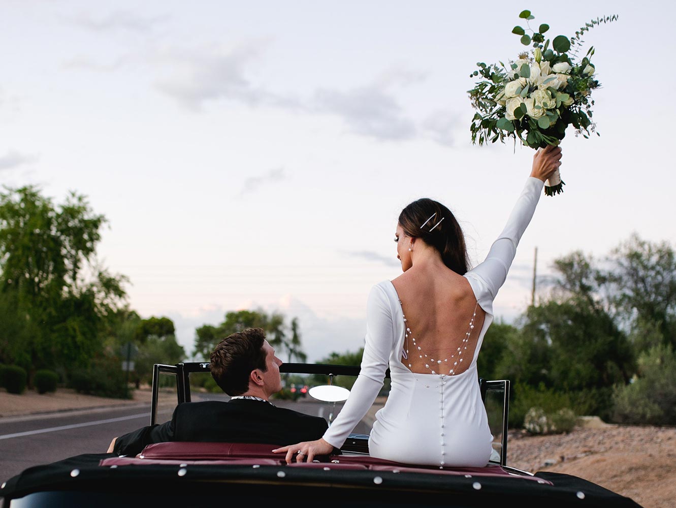 Jessica sits a top a convertable car holding up a bouquet with custom  crystal back necklace