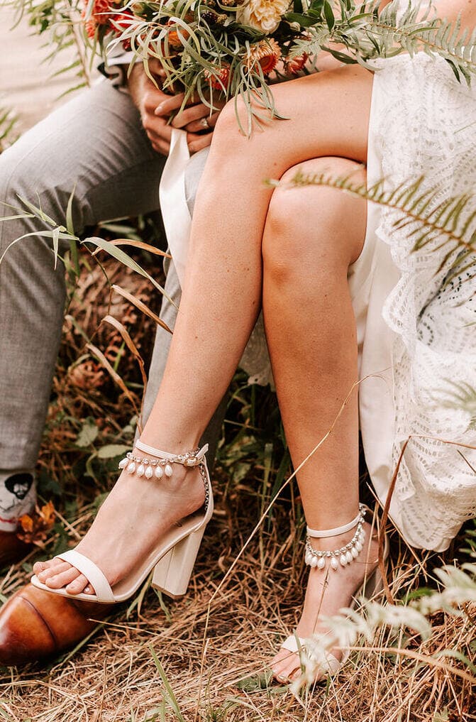 Jonika sits cross legged with bouquet wearing Khaleesi anklets with beige wedge heels