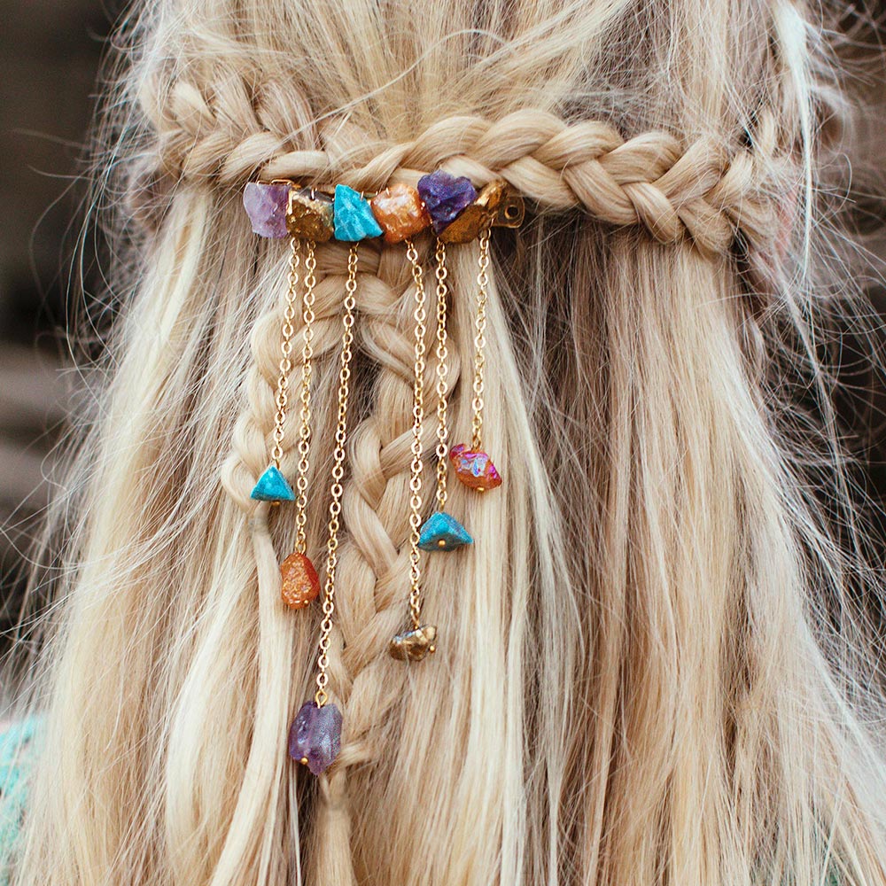 Close-up of a bohemian hairstyle from behind featuring blonde hair styled in braids, adorned with Raye multi-coloured decorative hair clip. The clip is embellished with colorful raw gemstones, a mix of including amethyst, apatite and crystal quartz, dangling from gold chains for a whimsical, natural look.
