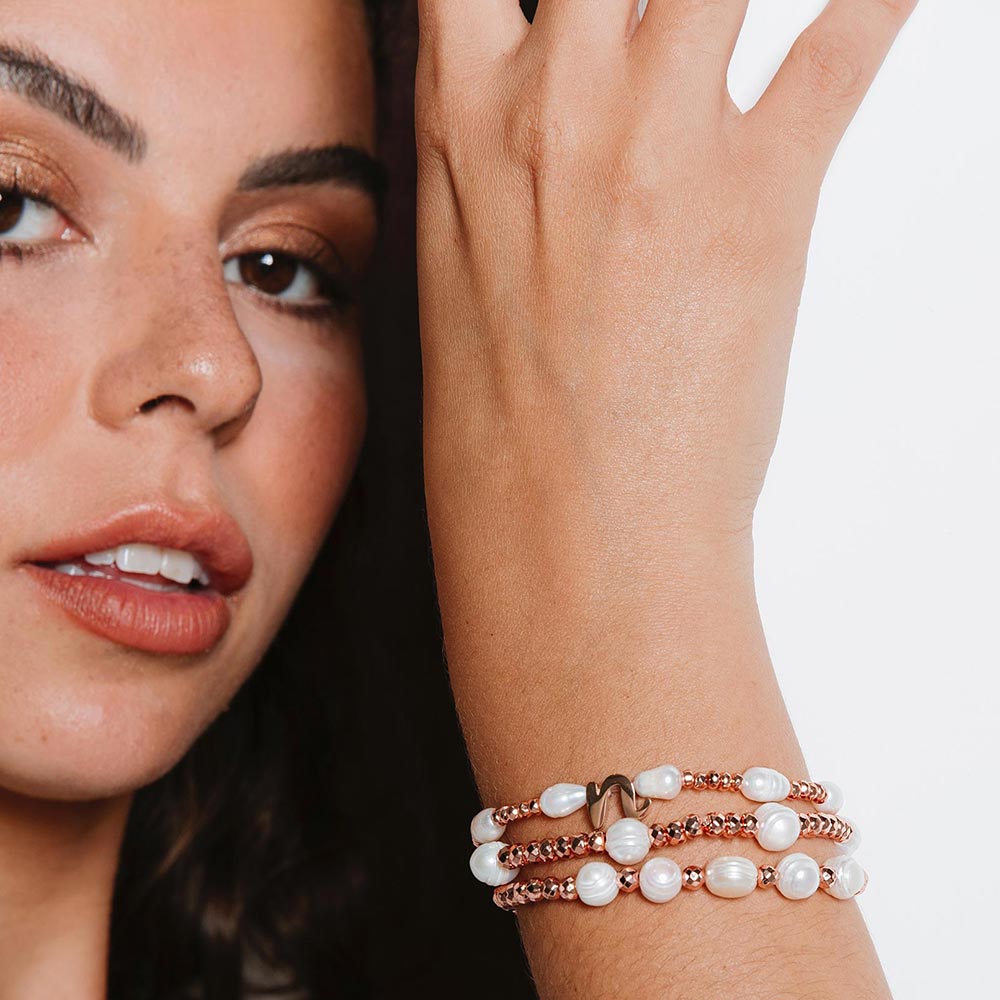 Tarni pearl and rose gold initial bracelet set of three worn on right arm close up.
