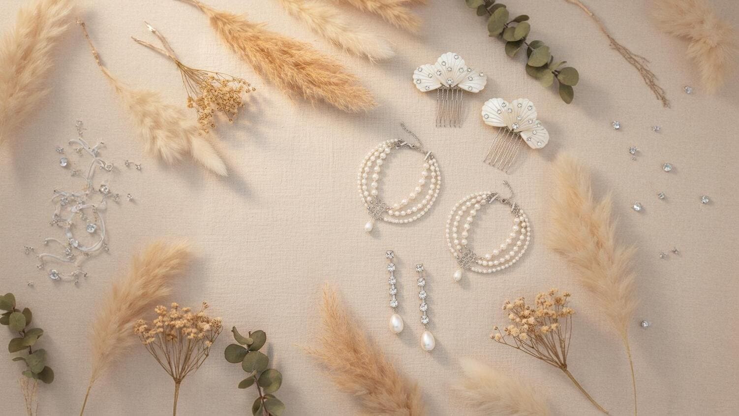 Pearl jewelry including earrings and a hair comb on a boho background with dried plants.