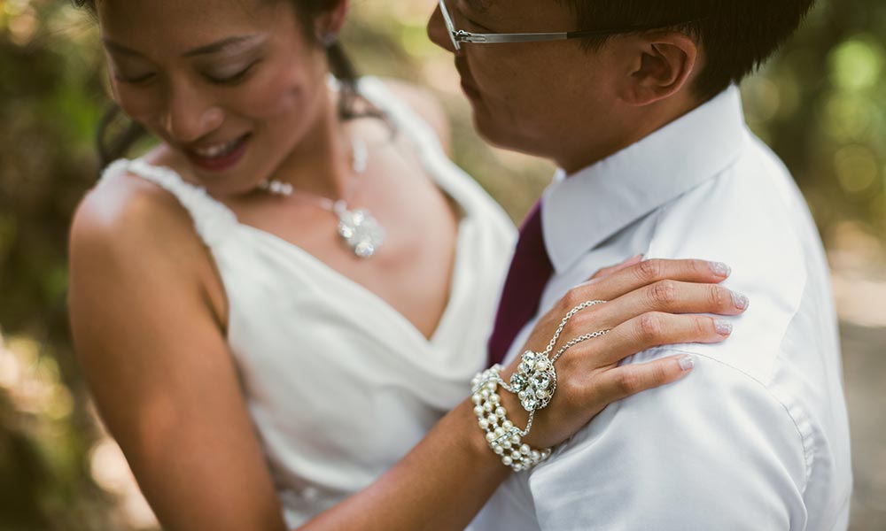 Bride wearing custom bracelet and necklace being embraced by husband