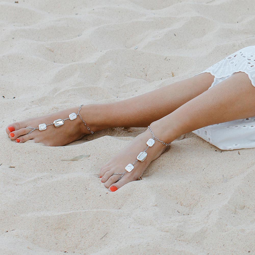 Leora boho pearl barefoot sandals in silver with white dress lying on sand