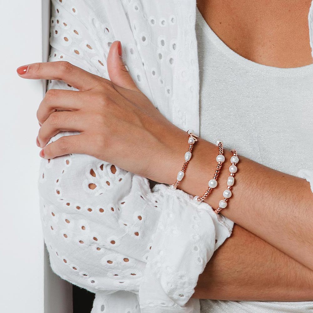 Tarni pearl and rose gold inital bracelet set of three worn on left arm crossed over.