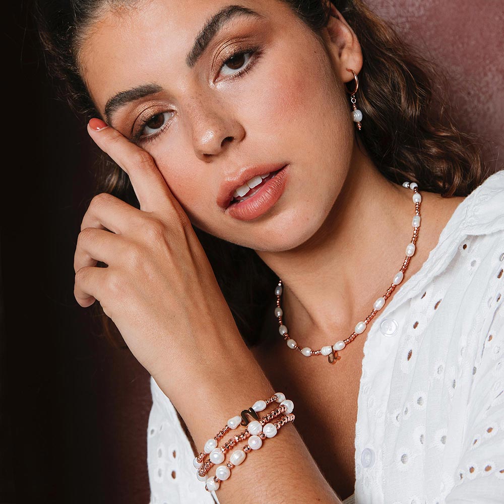 Tarni pearl and rose gold inital bracelet set of three worn on left hand up at side of face.