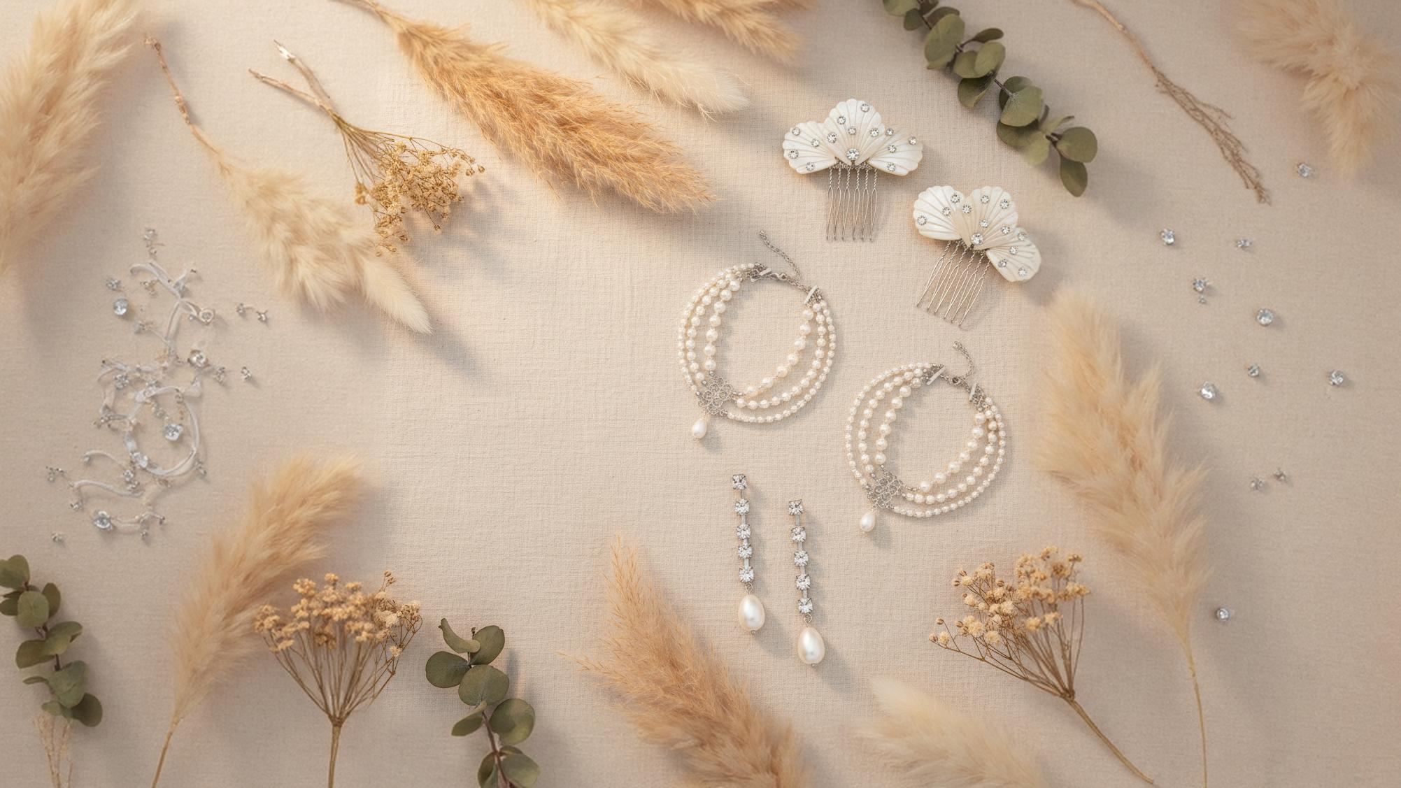 Pearl jewelry including earrings and a hair comb on a boho background with dried plants.