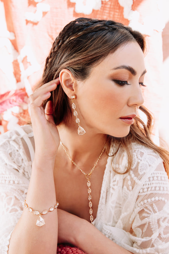 Brushing hair behind right ear wearing Faven crystal and gold earring, necklace and bracelet