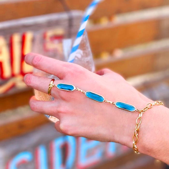 Azaria gold bracelet ring chain, teal crystal bracelet ring on hand holding drink.