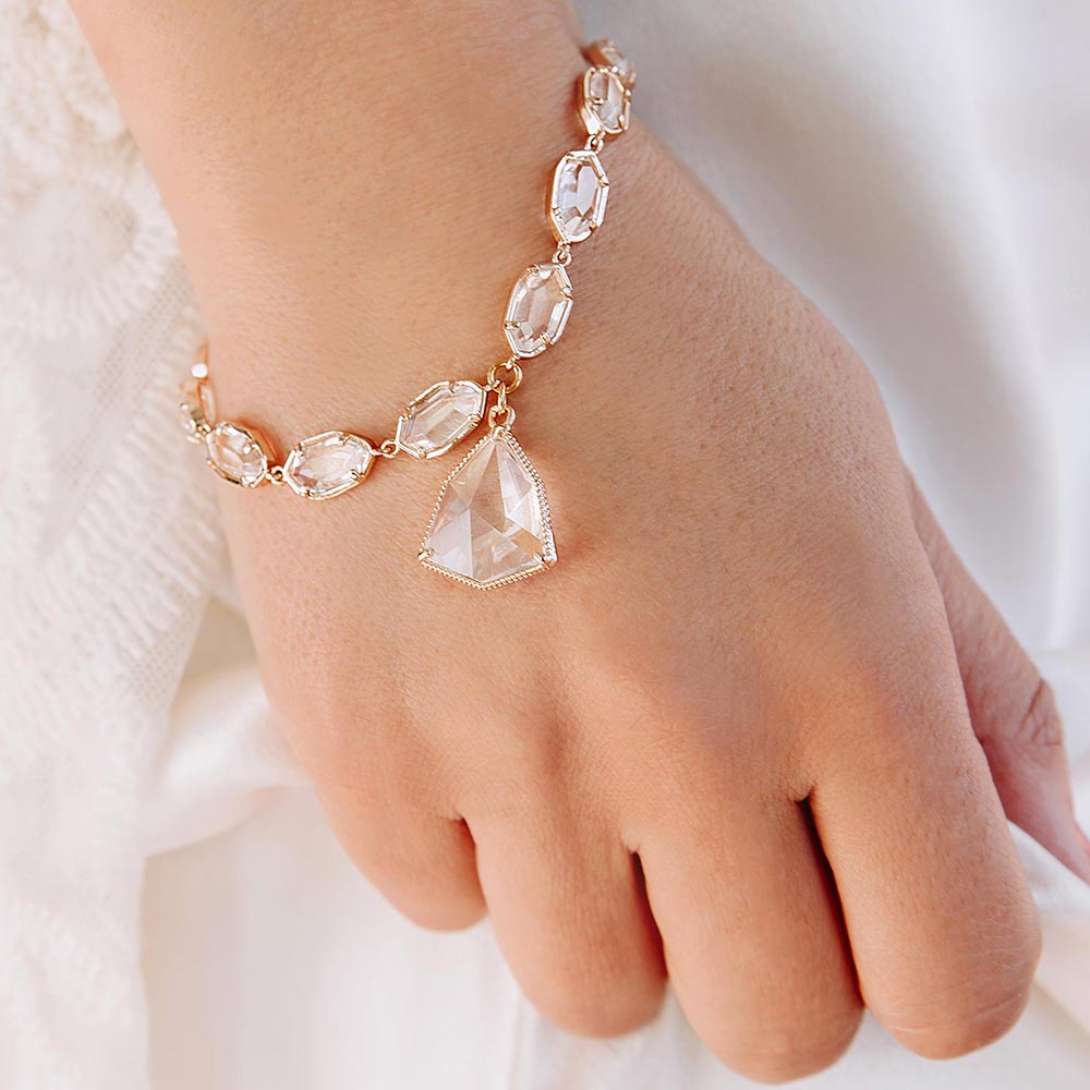 Faven gold and crystal bracelet on right hand holding white dress bridal style