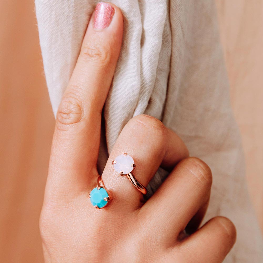 Close up of Jayda pink and turquoise Swarovski crystals ring set in rose gold side worn on right hand holding curtain