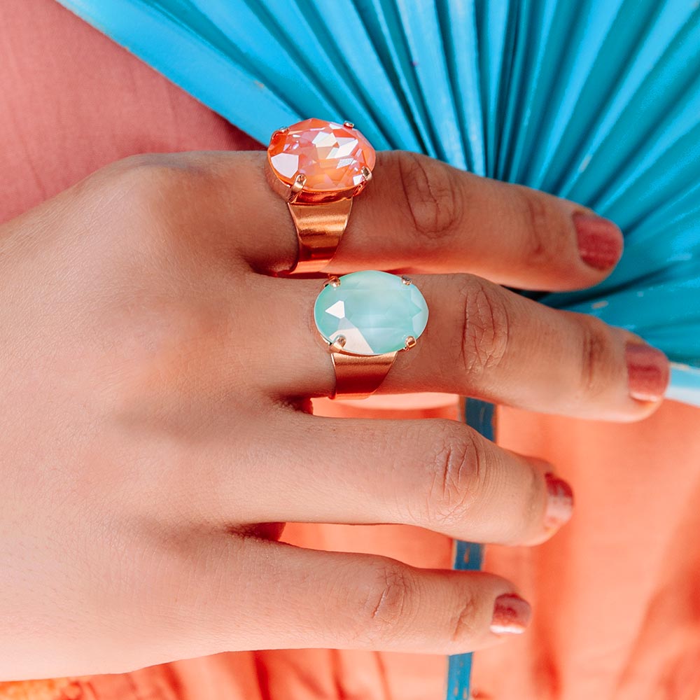 Mia large colourful crystal rose gold rings mint and orange, hand holding fan.
