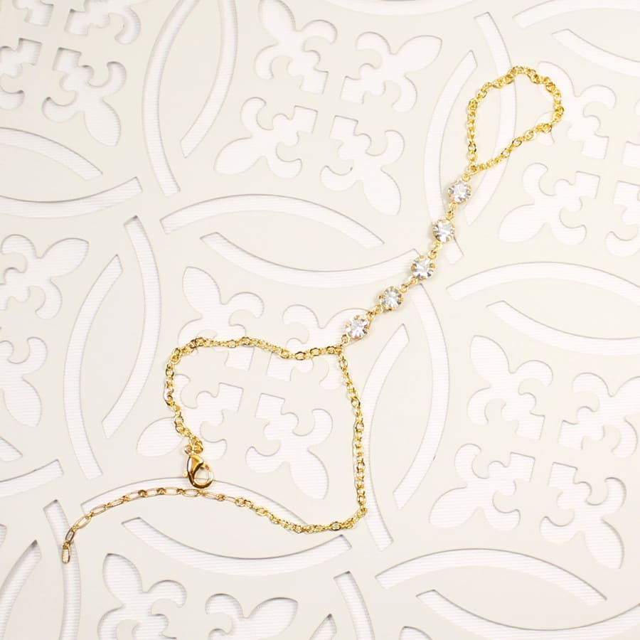 Alek crystal hand chain bracelet in gold colour on patterned tile background