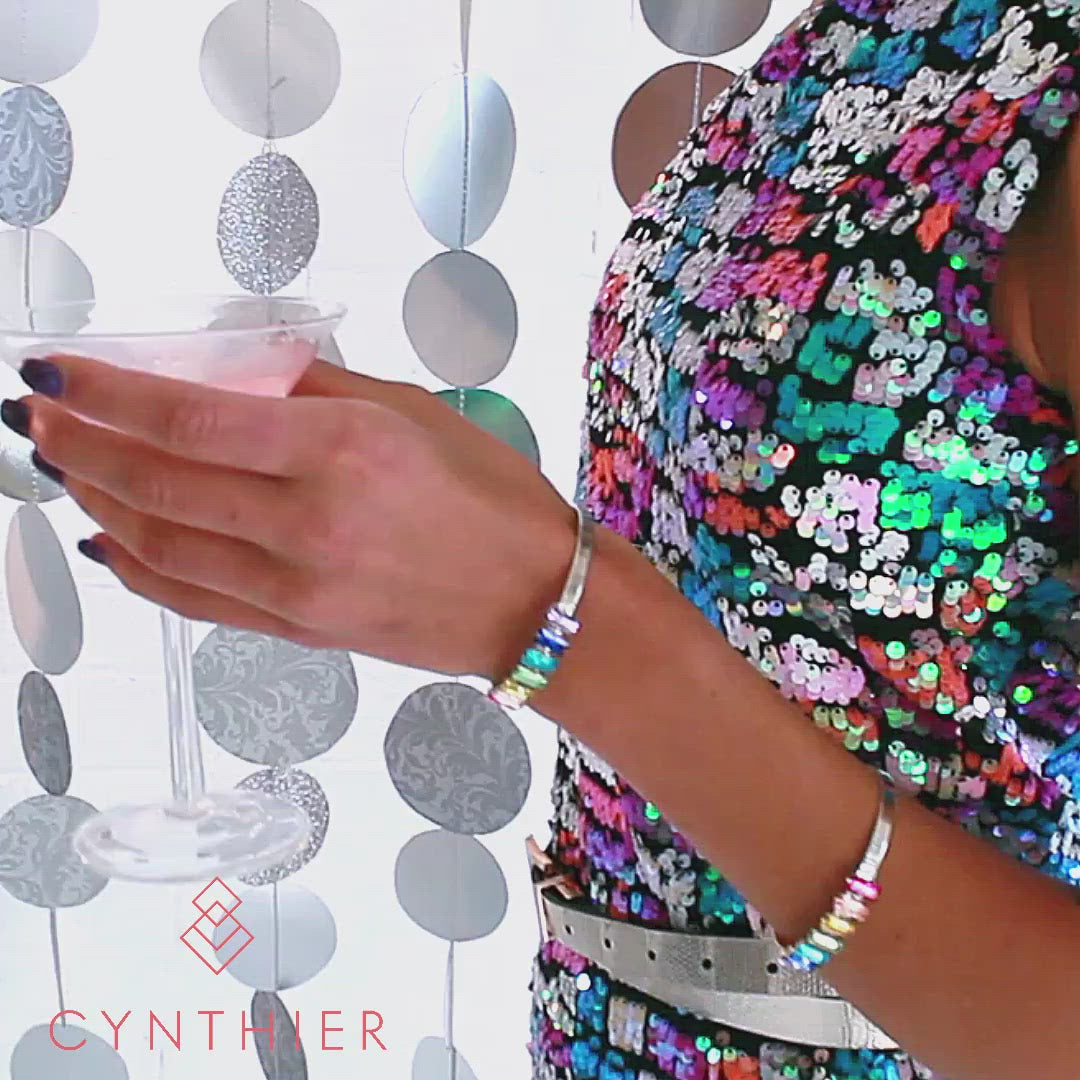 Woman wearing Billie rainbow crystal bangles and Billie rainbow crystal earrings whilst sipping on a cocktail.