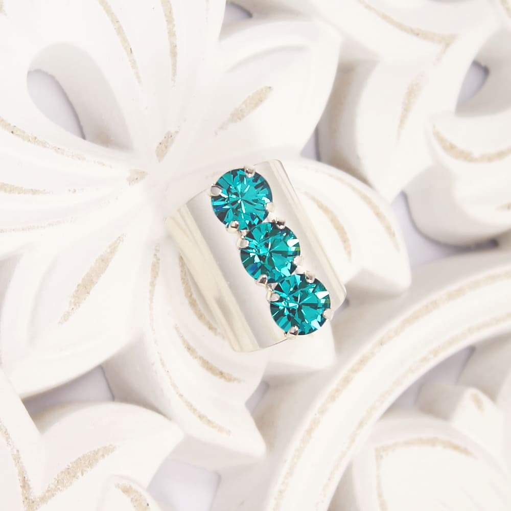 Simone three crystals statement ring Silver with Blue Zircon on white floral plate.